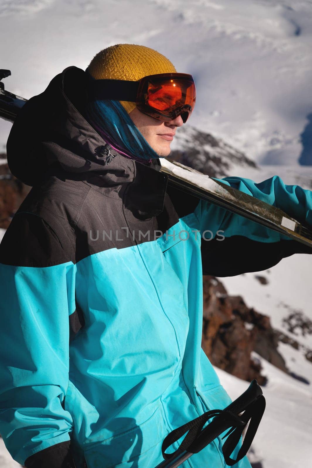 young male skier in ski goggles stands with skis on his shoulder ready for competition. sportsman portrait by yanik88