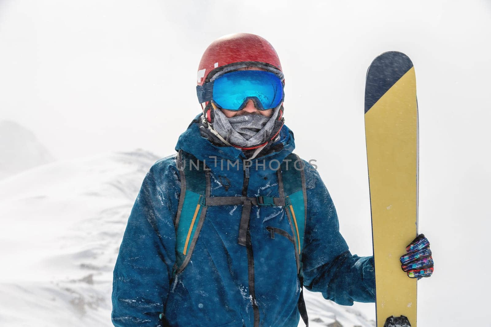 Happy skier stands on the mountain. Skier holding skis and looking at the camera on the background of a snowy valley by yanik88