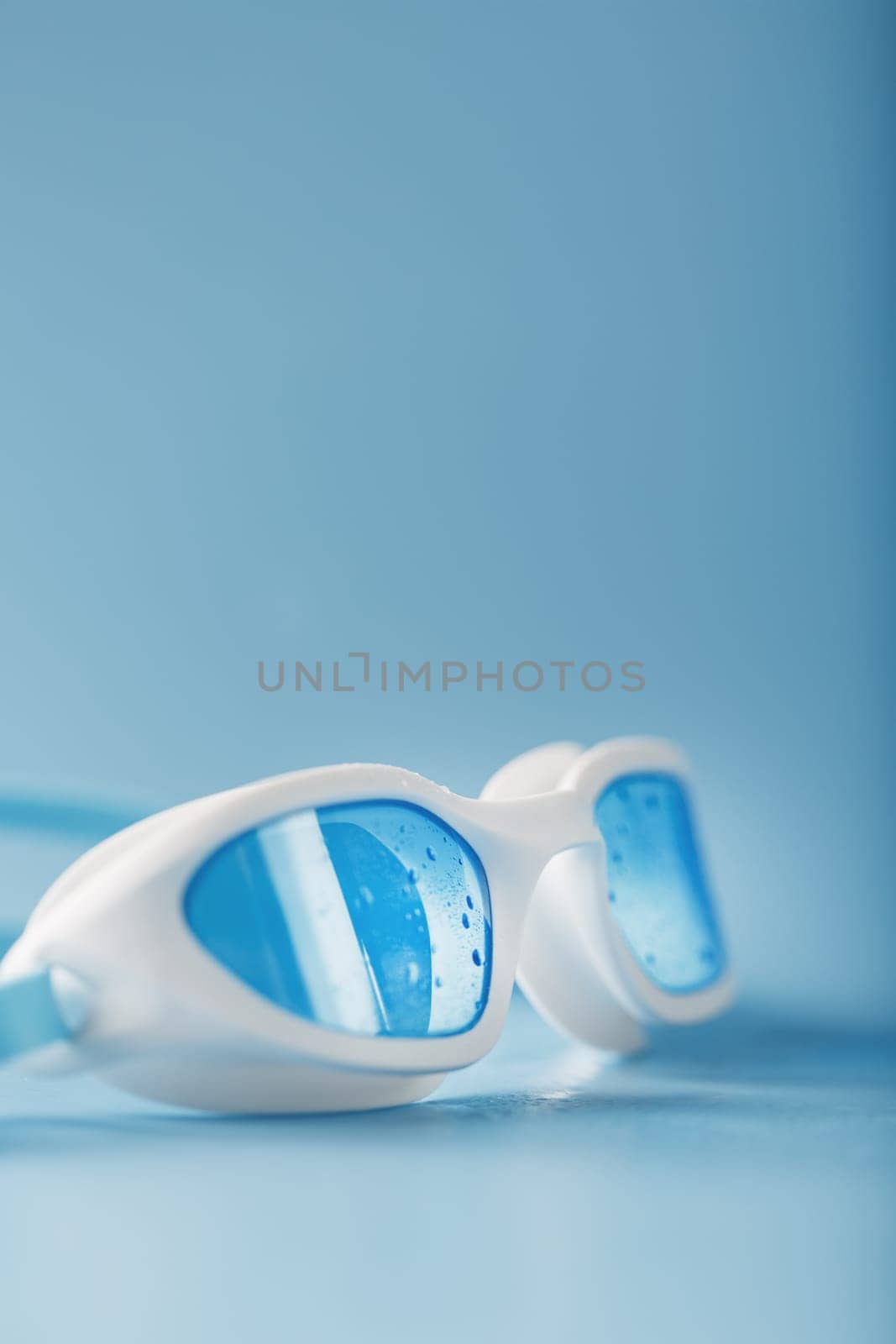 White swimming glasses with a blue lens on a blue background