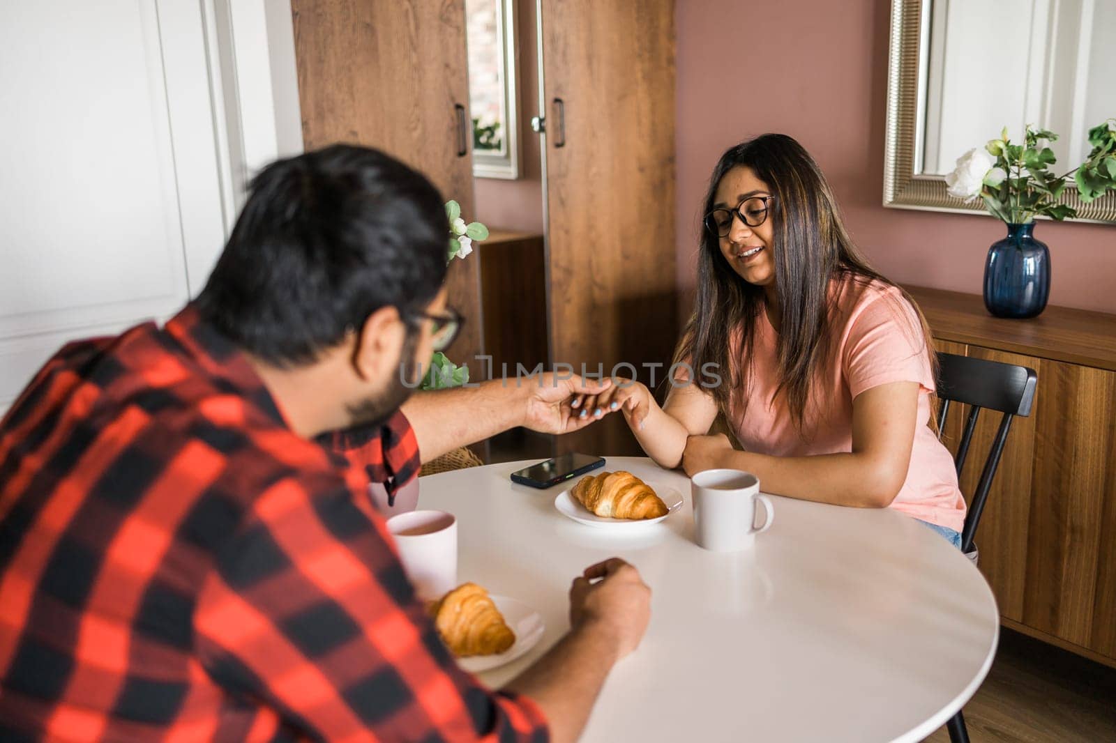 Young diverse loving couple eating croissant and talks together at home in breakfast time. Communication and relationship