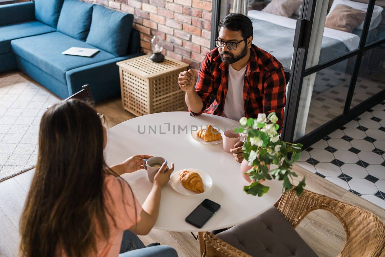 Young diverse loving couple eating croissant and talks together at home in breakfast time. Communication and relationship concept by Satura86