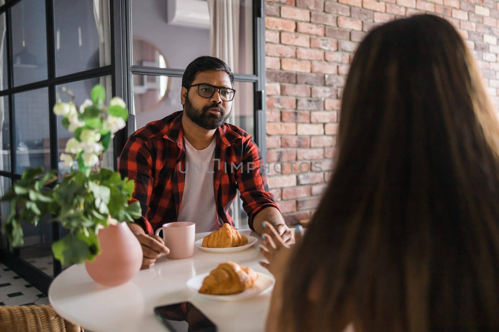 Young diverse loving couple eating croissant and talks together at home in breakfast time. Communication and relationship