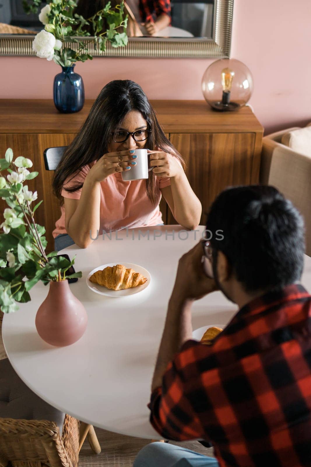 Happy couple eating breakfast and talking at dining table in morning. Indian girl and latino guy. Relationship and diversity concept by Satura86