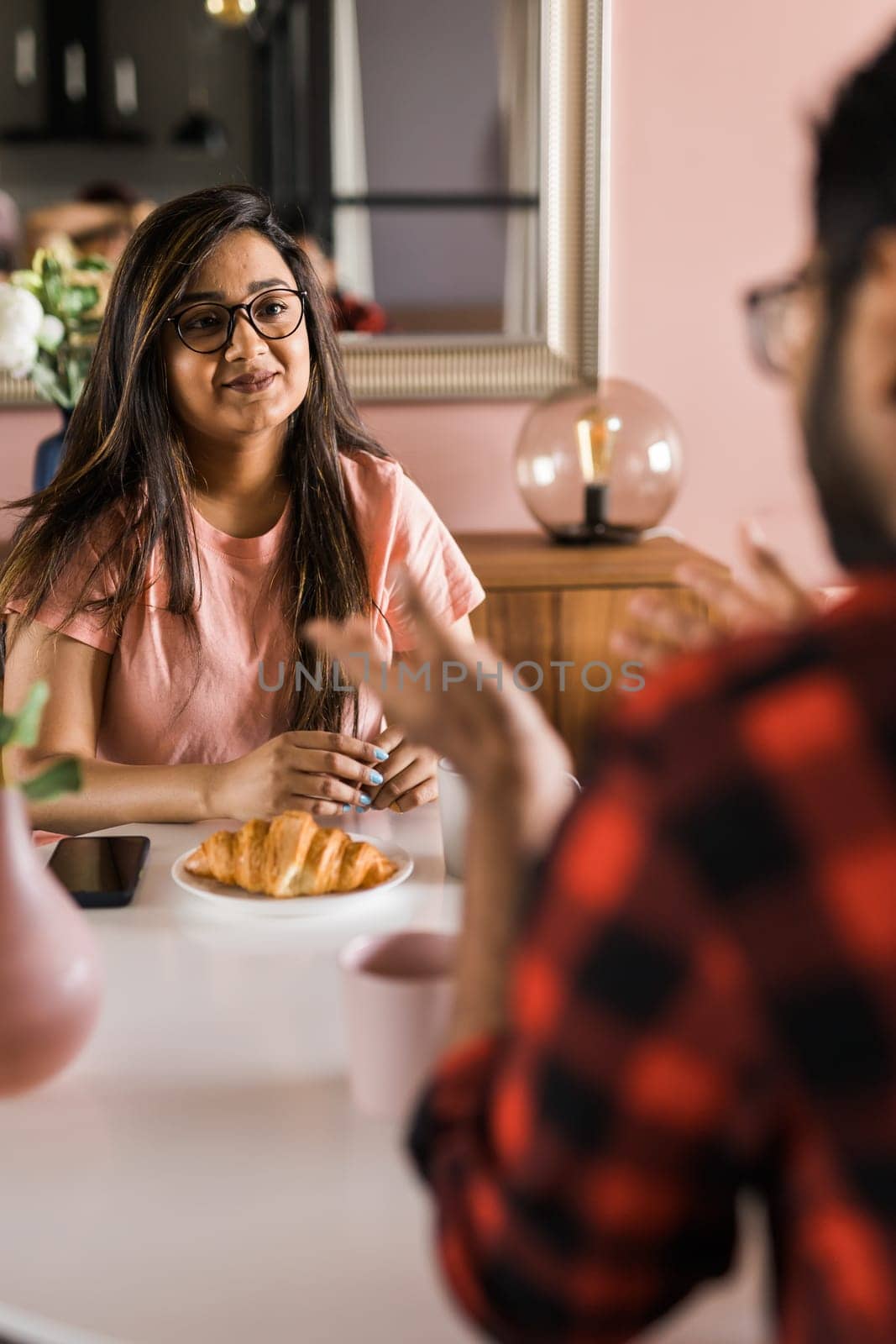 Happy couple eating breakfast and talking at dining table in morning. Indian girl and latin guy. Relationship and diversity