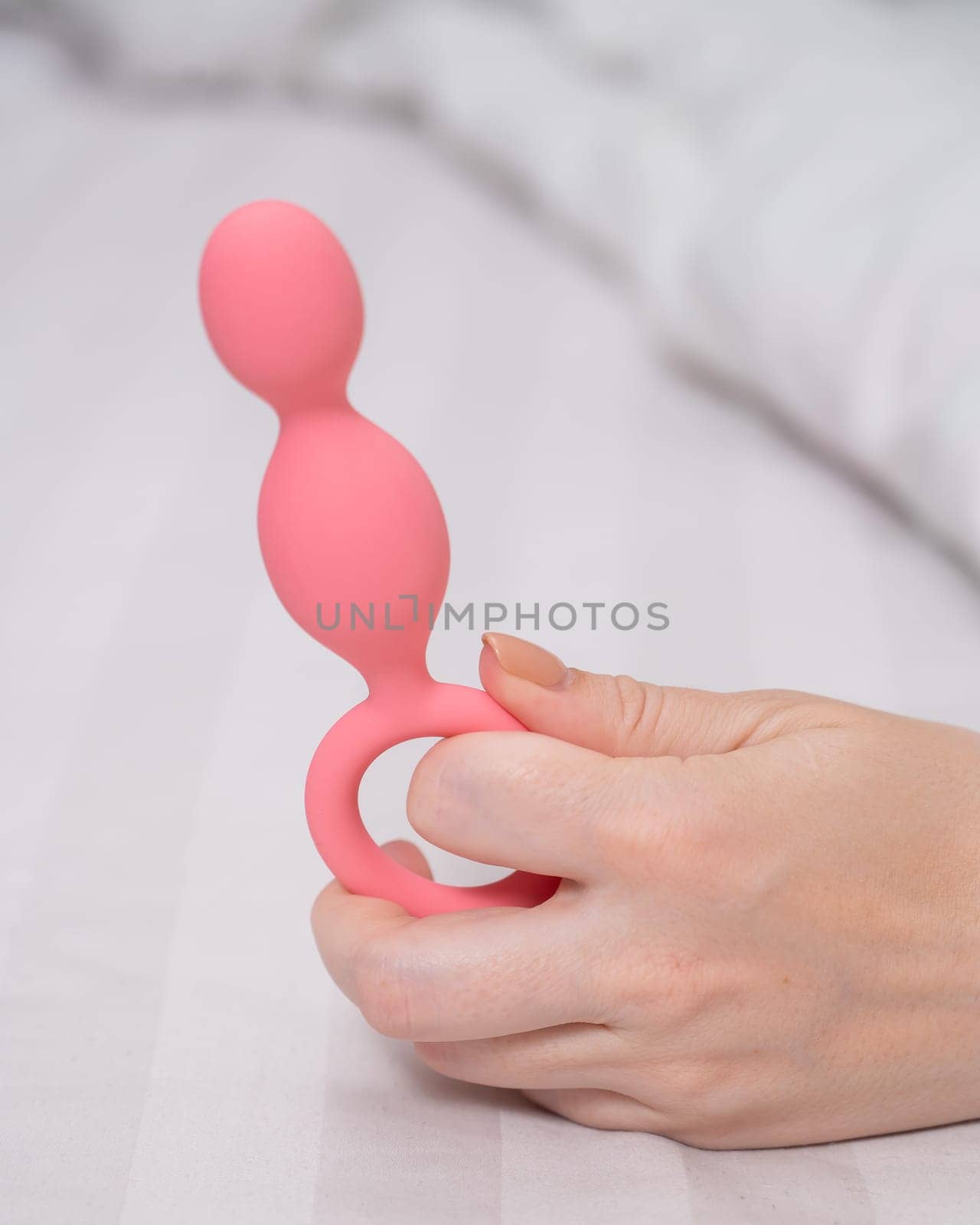 Close-up of a female hand with pink anal beads lying in bed. by mrwed54