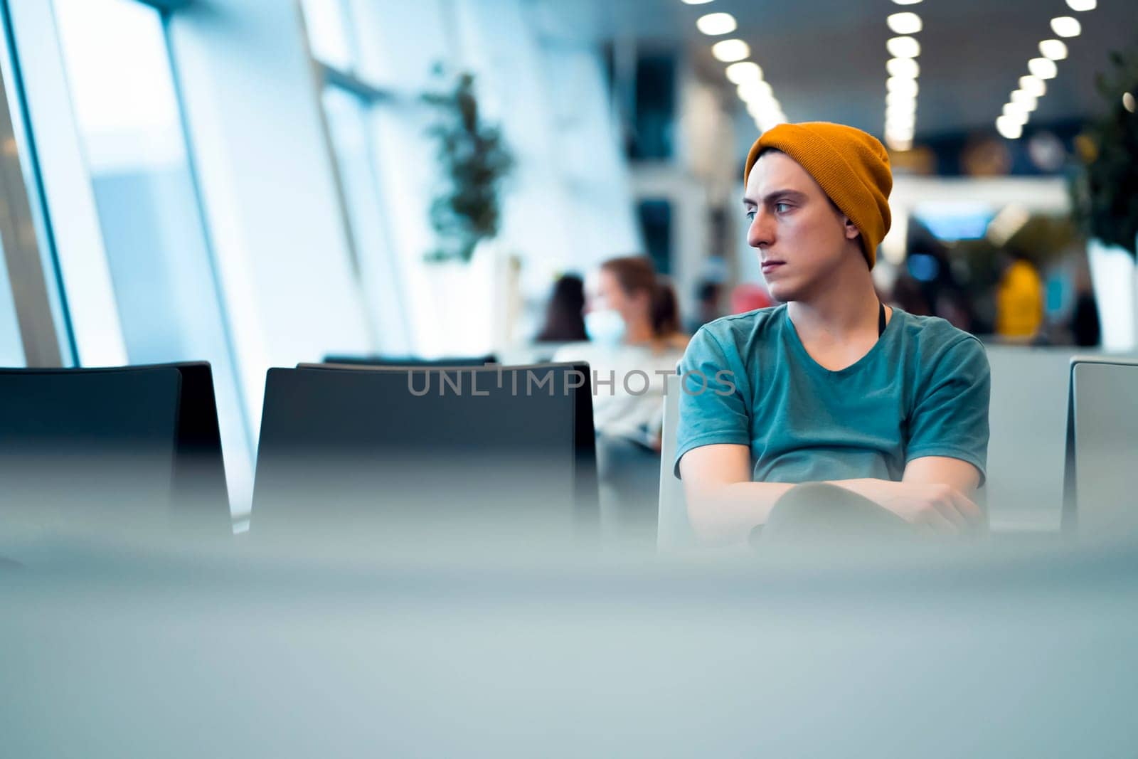 A young man in casual clothes sits at the airport waiting hall, waits for the plane while traveling, is in the transit area before arrival or departure.