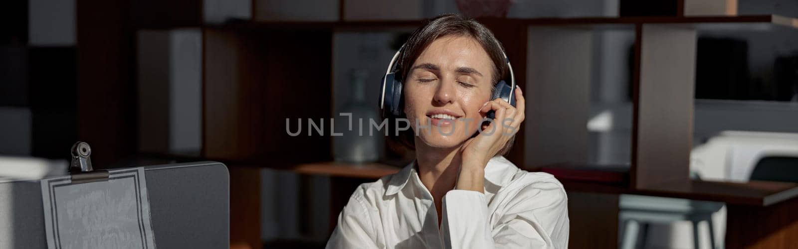 Attractive business woman in headphones listen music while working laptop sitting in cozy cafe by Yaroslav_astakhov