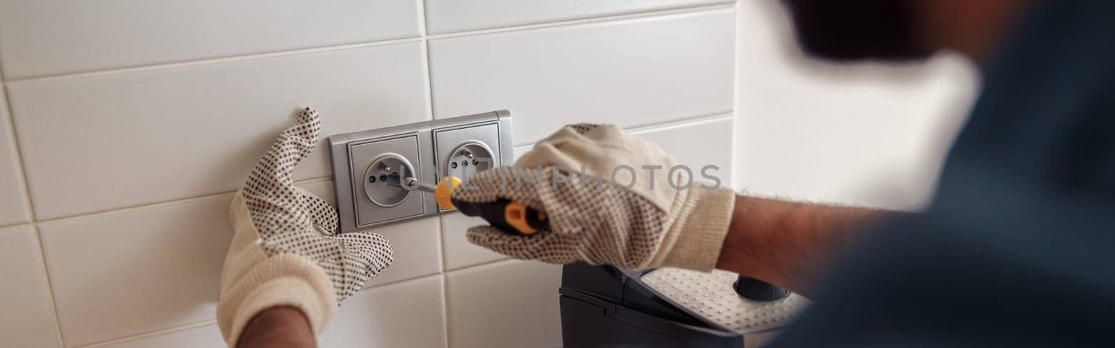 Professional electrician worker in uniform with screwdriver is repairing power socket in kitchen