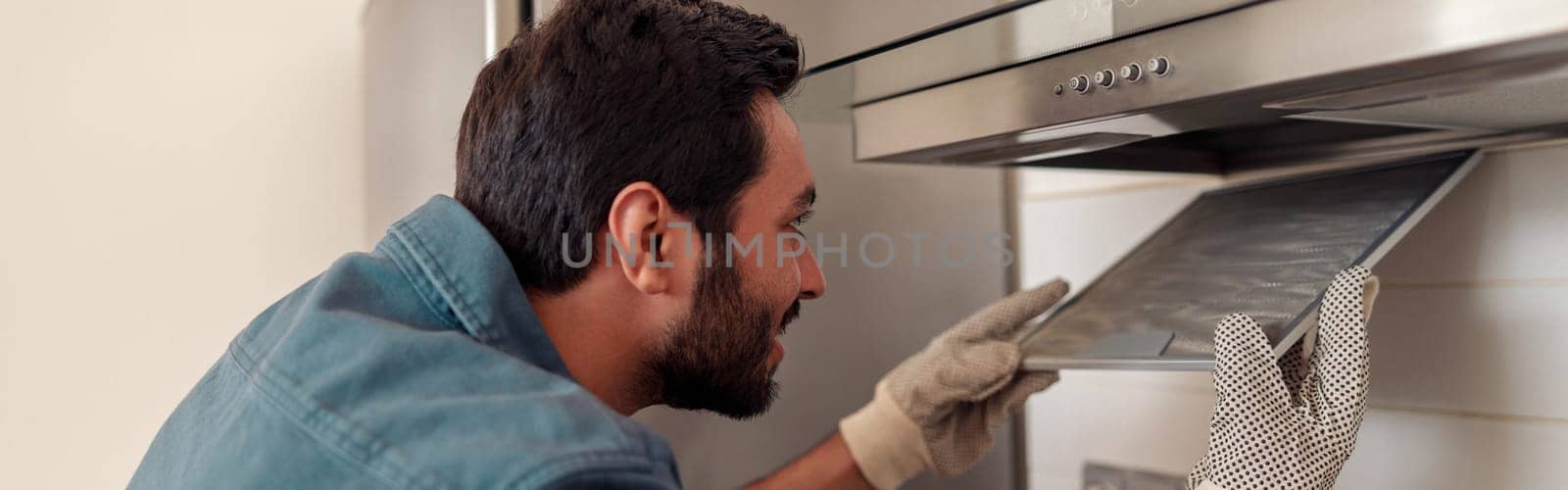 Handyman in uniform repairing kitchen extractor, replacing filter in cooker hood.Maintenance concept by Yaroslav_astakhov