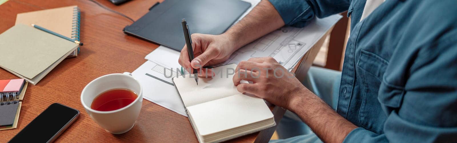 Close up of man hands making notes in notepad while sitting on his workplace. High quality photo