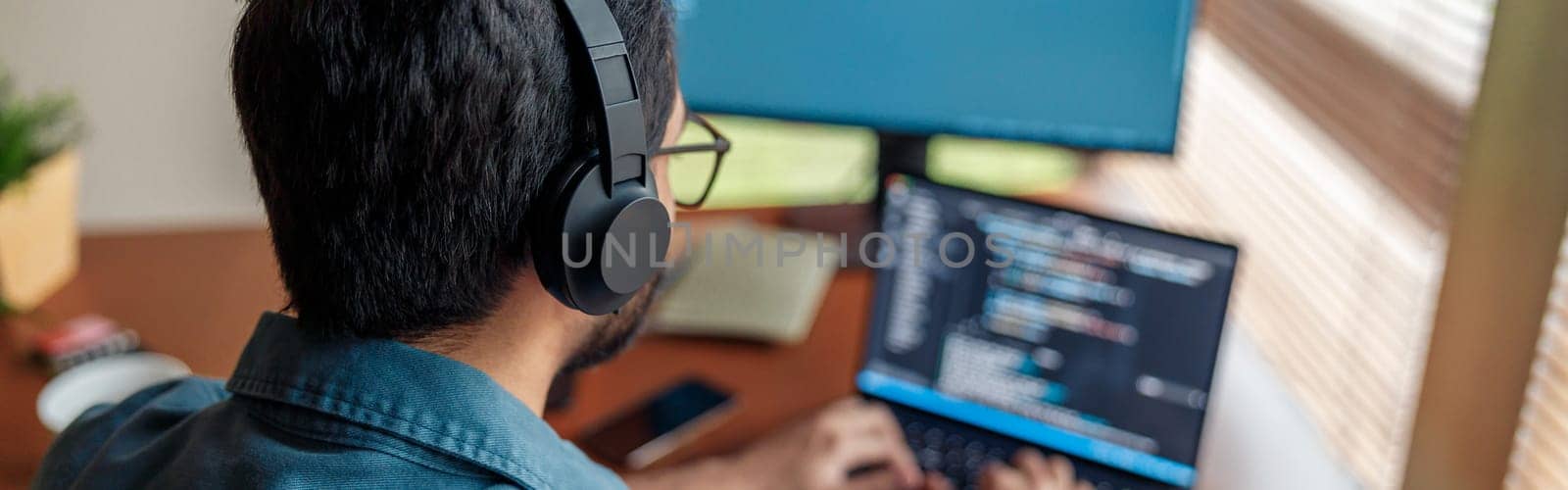 Back view of man in headphones freelance data scientist work remotely at home. High quality photo