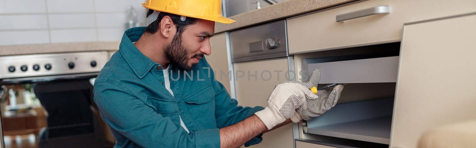 Male worker in uniform is assembling furniture on kitchen. Repair concept. High quality photo