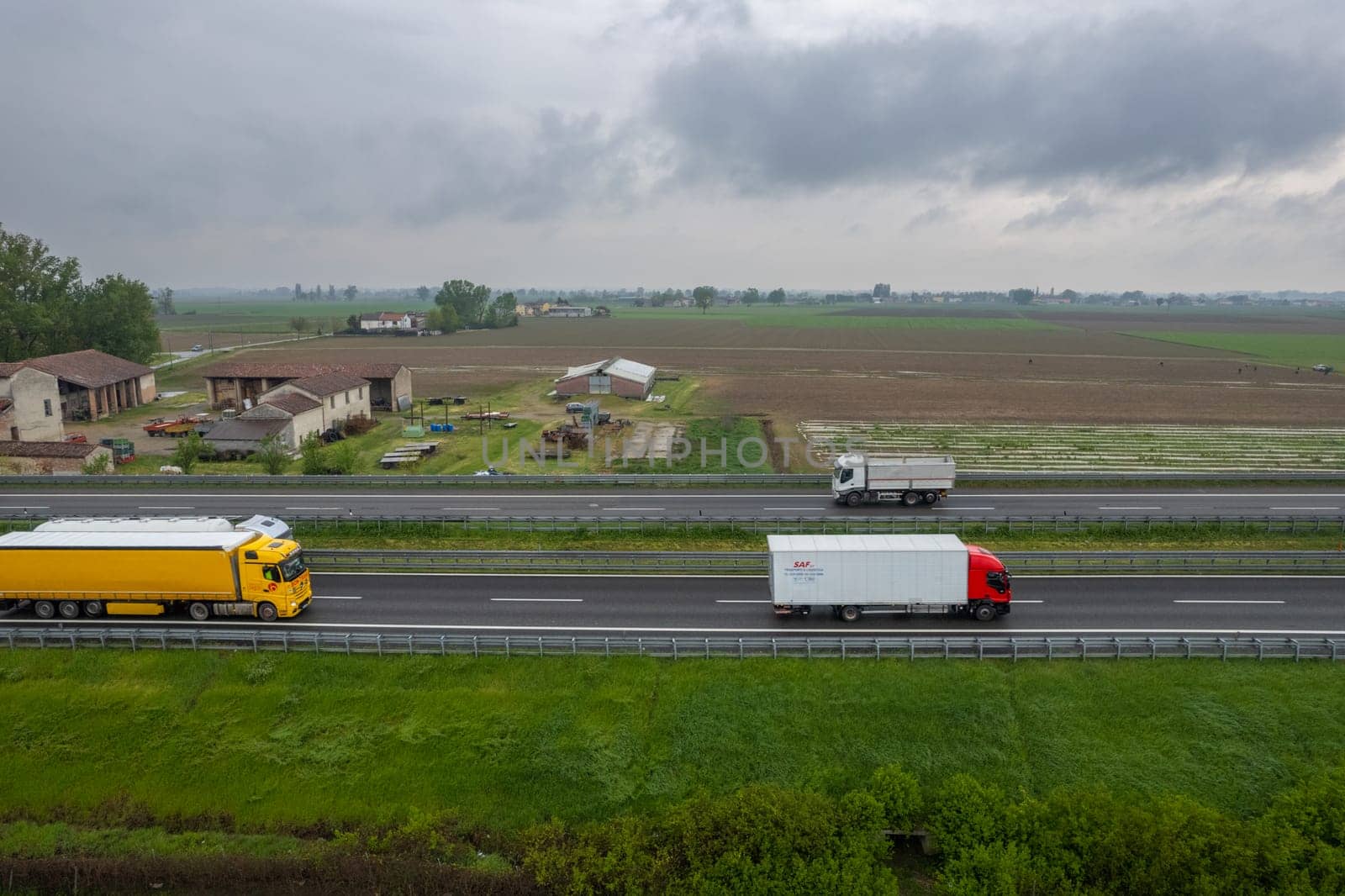 Piacenza, Italy - April 2023 Cargo trucks and cars in the motorway a1 autostrada del sole aerial point of view in between padain plain rural fields