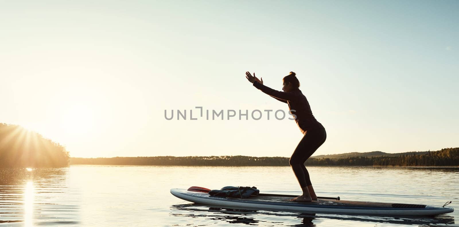 The new way to do yoga. an attractive young woman doing yoga on a paddle board on a lake outdoors. by YuriArcurs