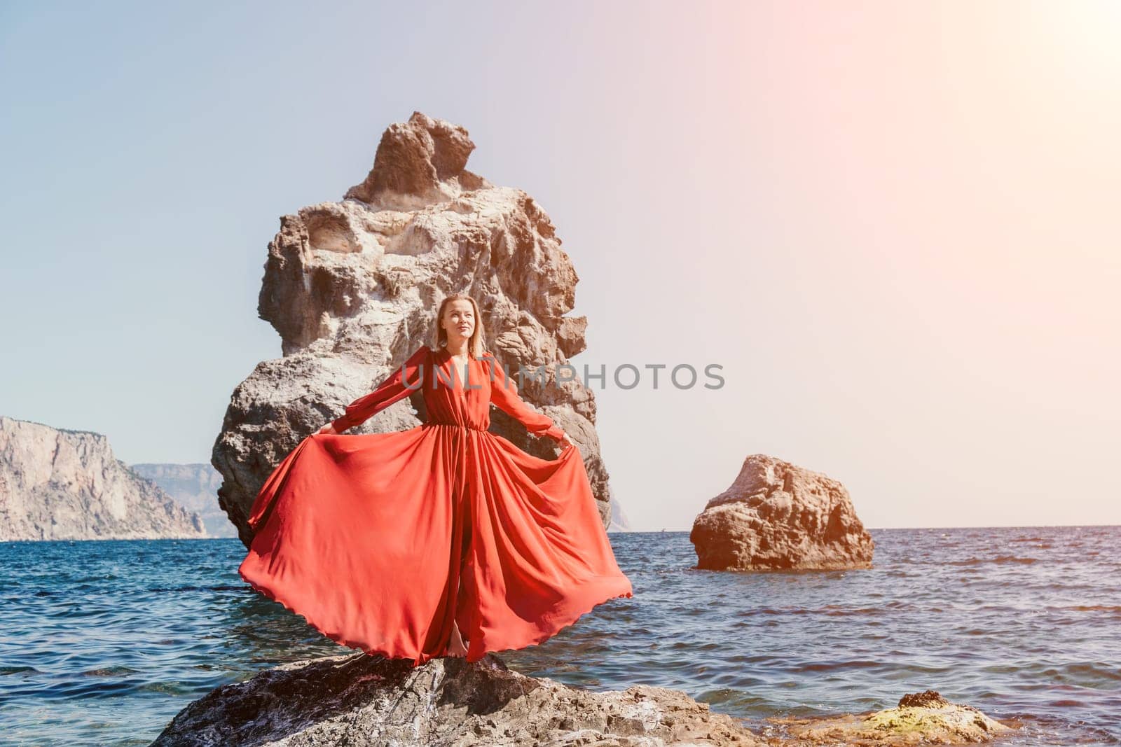 Woman travel sea. Young Happy woman in a long red dress posing on a beach near the sea on background of volcanic rocks, like in Iceland, sharing travel adventure journey