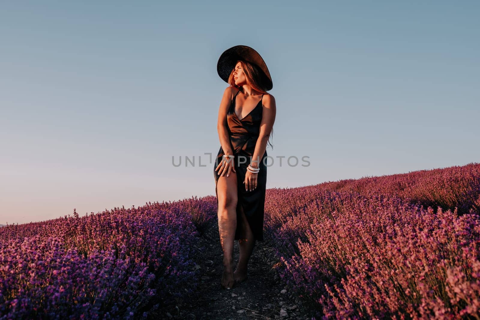 Woman lavender field. Happy carefree woman in black dress and hat with large brim walking in a lavender field during sunset. Perfect for inspirational and warm concepts in travel and wanderlust. by panophotograph