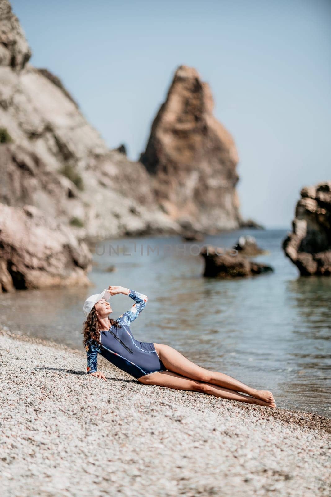 Portrait woman sea. Well looking middle aged woman with black hair, fitness instructor in blue swimwear on the rocky beach near the sea. Female fitness yoga routine concept. Healthy lifestyle. by panophotograph