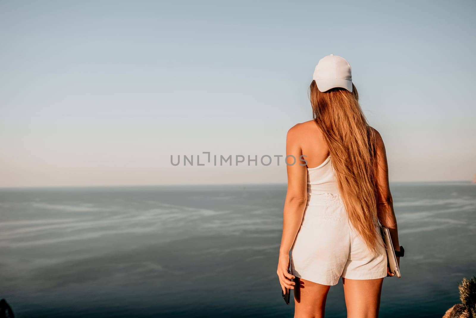 Woman laptop sea. Working remotely on seashore. Happy successful woman female freelancer in straw hat working on laptop by the sea at sunset. Freelance, remote work on vacation by panophotograph