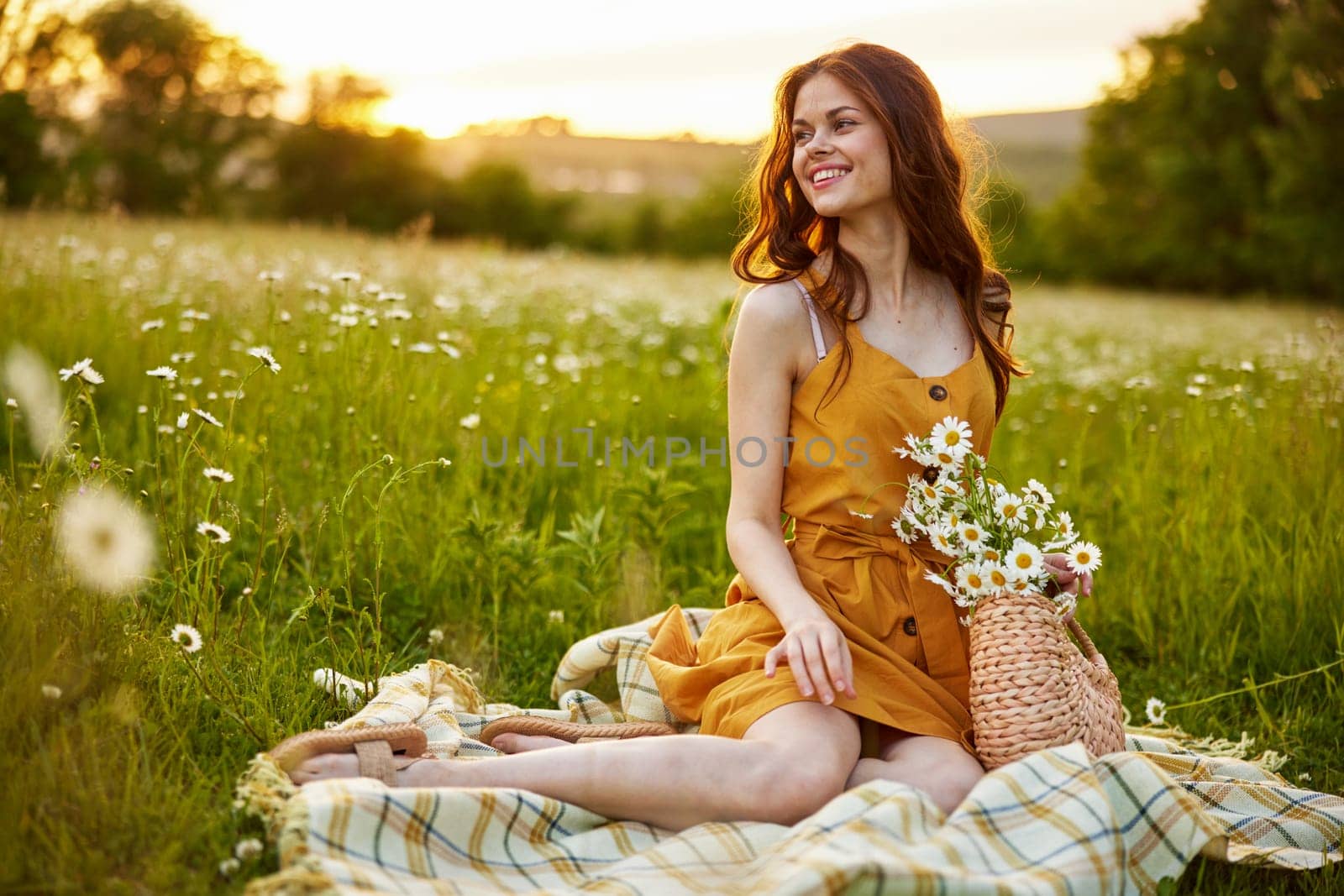 beautiful woman, in a summer orange dress enjoys nature while sitting in a chamomile field by Vichizh