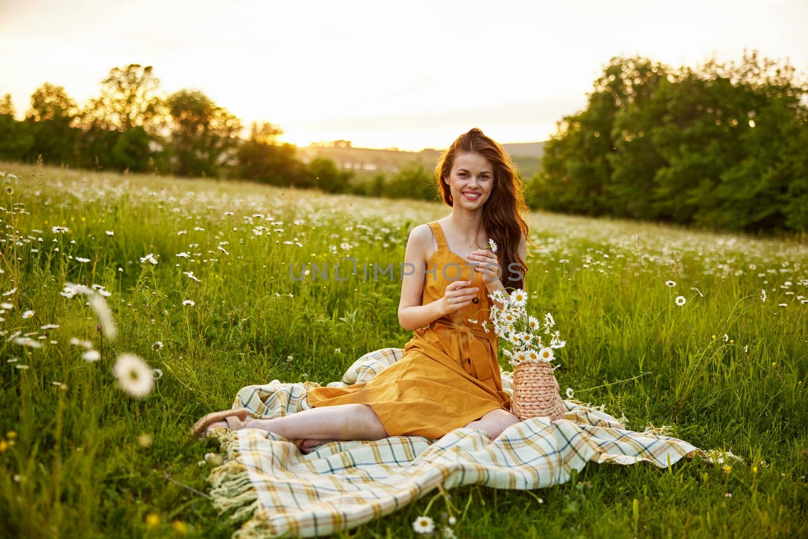 beautiful woman, in a summer orange dress enjoys nature while sitting in a chamomile field by Vichizh