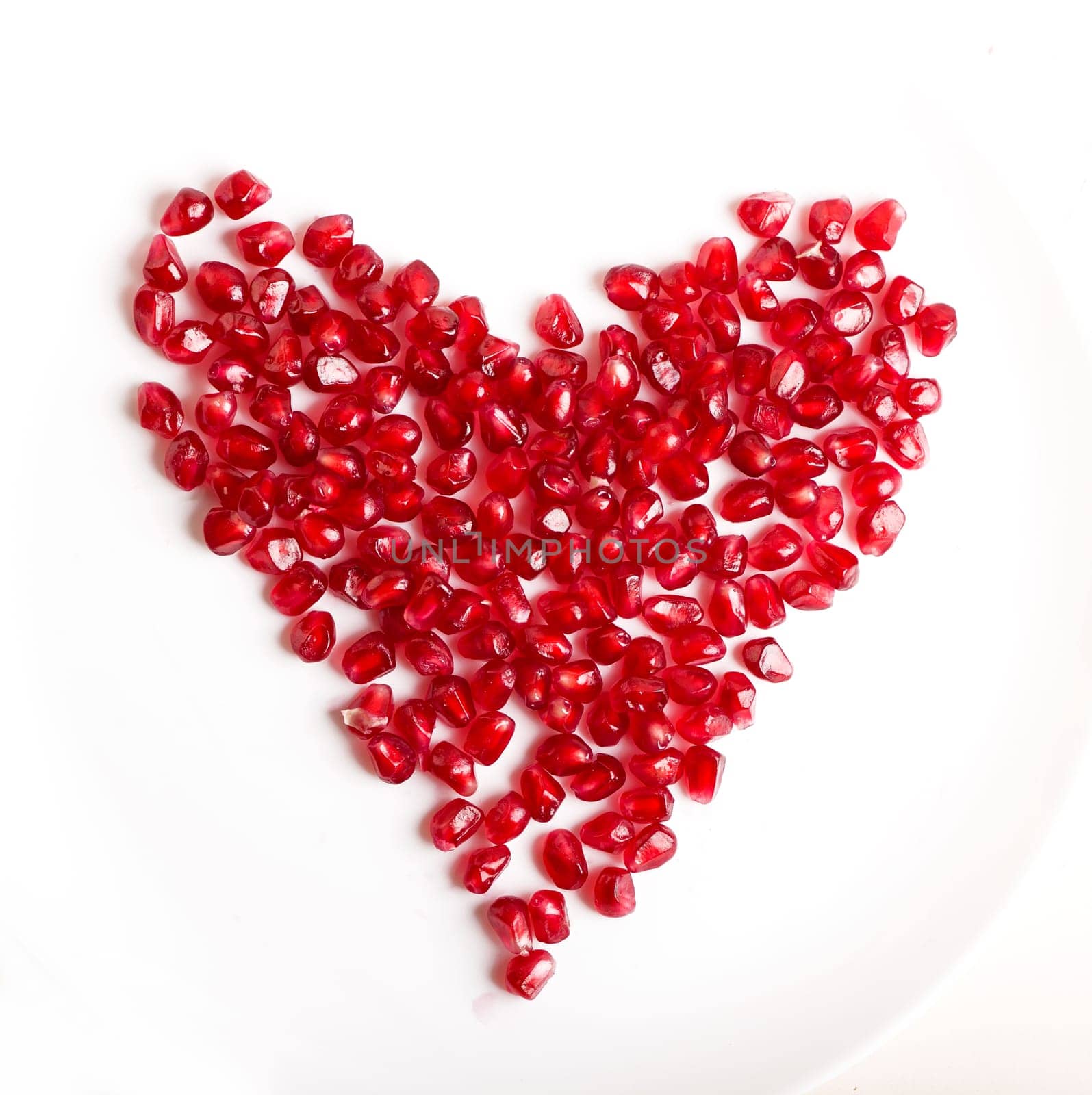 pomegranate seeds in the form of a heart on a white background. Cut the pomegranate with scattered grain top view isolated on white background. by aprilphoto
