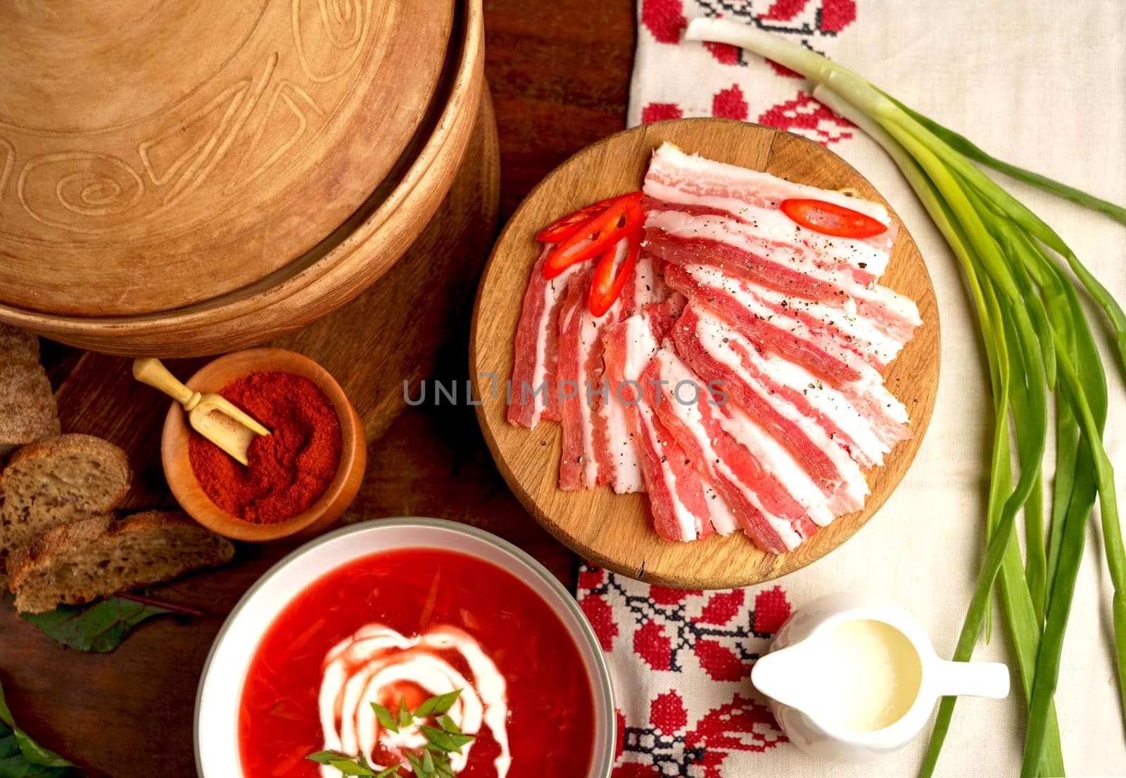 Traditional Ukrainian borsht, red vegetable soup or borscht with smetana on wooden background. Slavic dish with cabbage, beets, tomatoes Traditional Ukrainian towel along with garlic, bread and salt. Top view of a wooden tray on a black background on which lies Ukrainian food with spices by aprilphoto