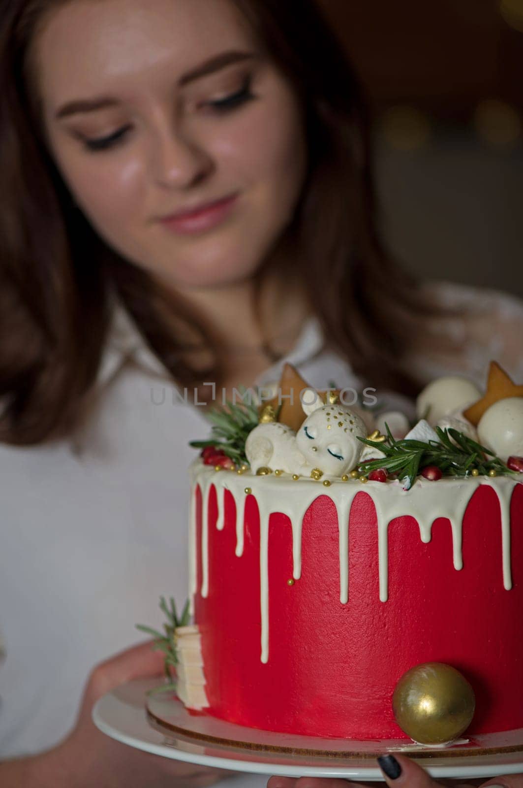 A beautiful happy girl in a white T-shirt, stands at home, holds a festive New Year's cake on a plate by aprilphoto