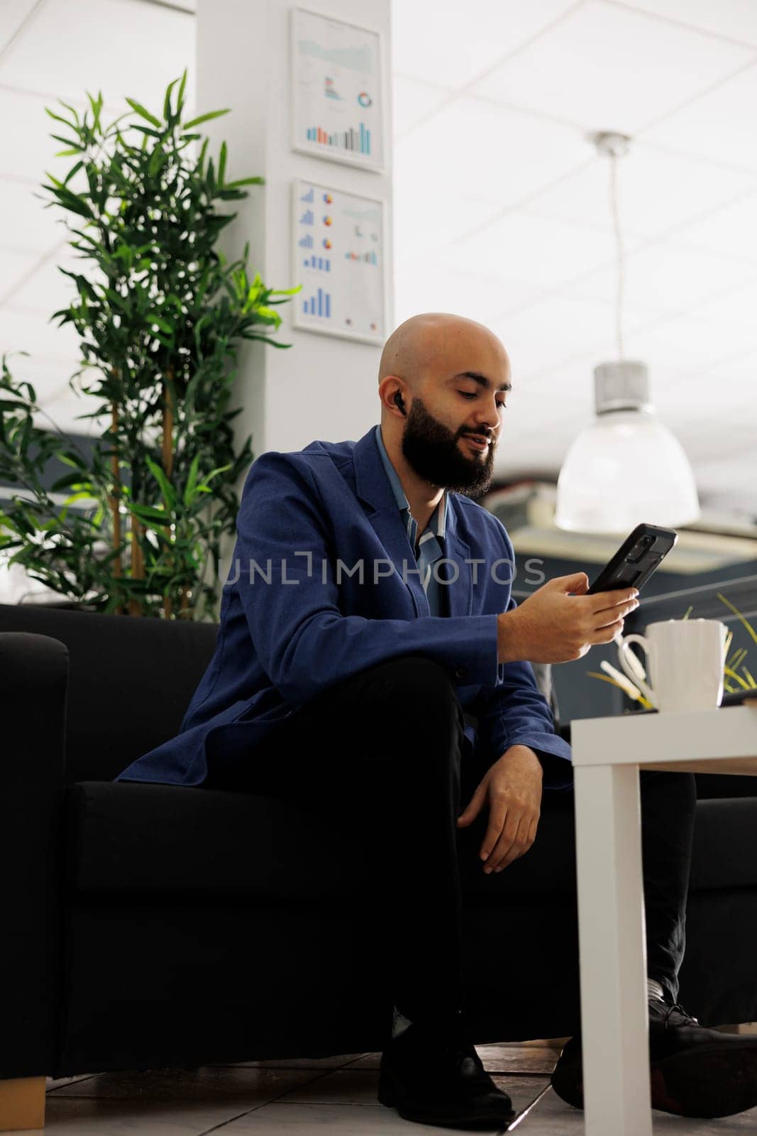 Company employee discussing business strategy on smartphone video conference. Arab professional sitting on couch and having online communication with remote team in office
