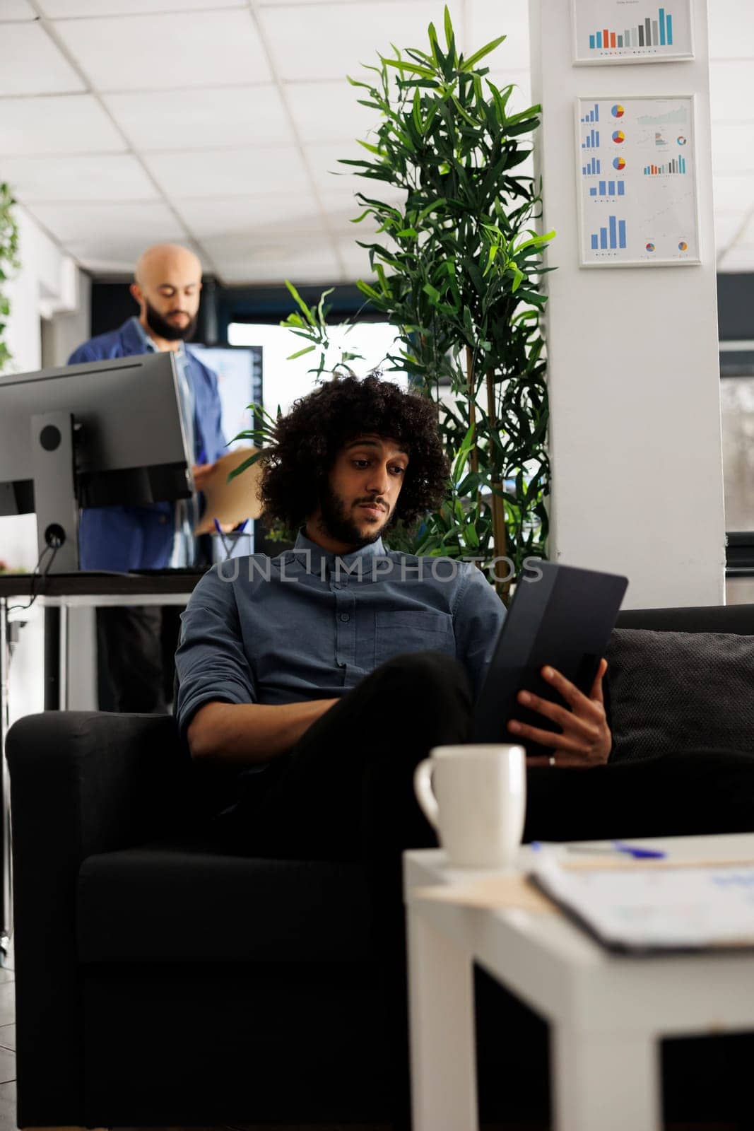 Unicron business professional using digital table during work break in start up office. Entrepreneur watching video on portable gadget while sitting on couch in modern coworking space