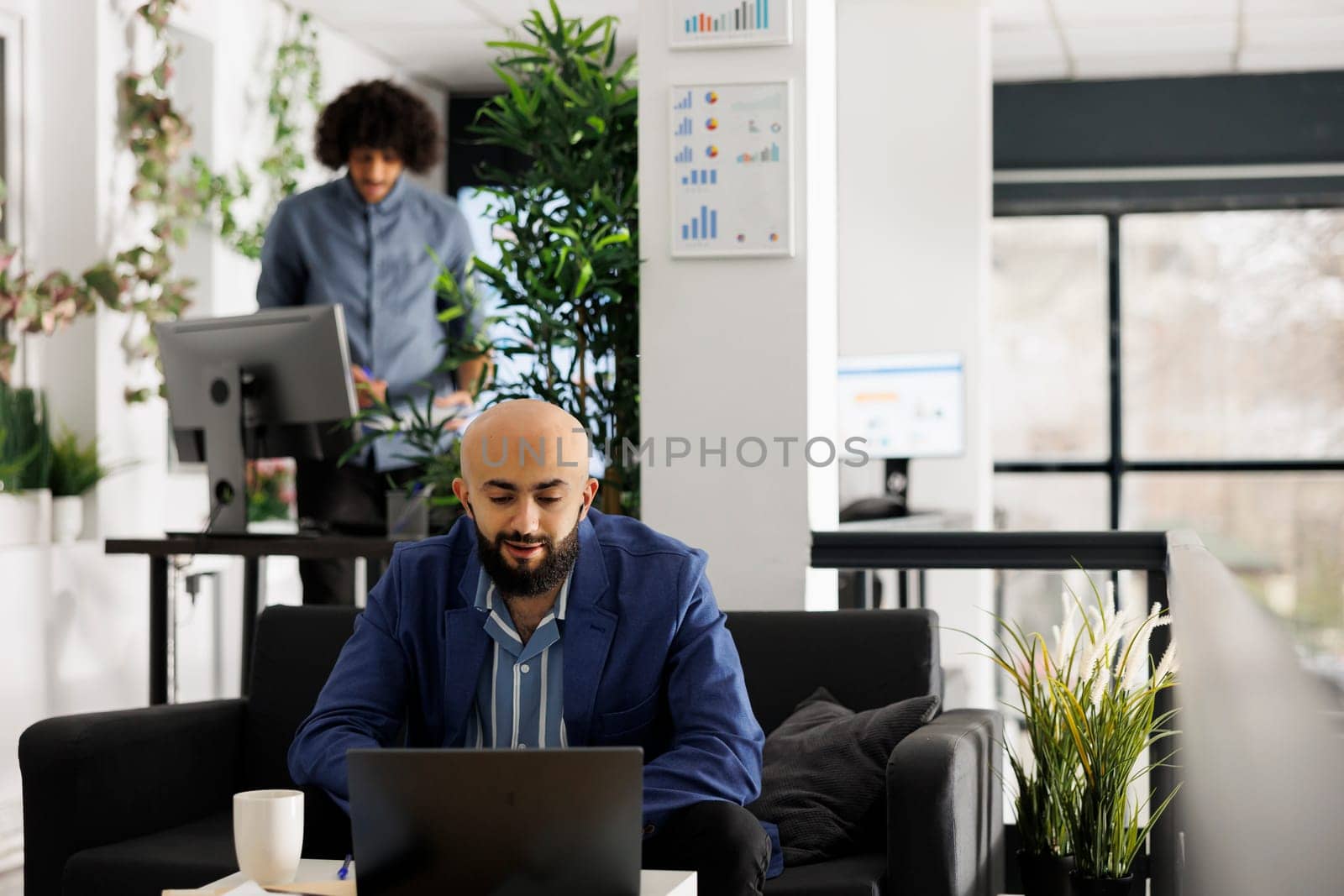 Arab company employee discussing start up in videocall with remote team in business office. Young man entrepreneur having online communication with coworkers using laptop in open space