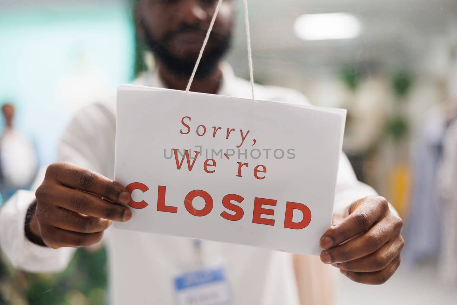 African American clothing shop assistant hands holding sorry we are closed sign. Fashion apparel store seller arms hanging information sign on entrance door at end of day