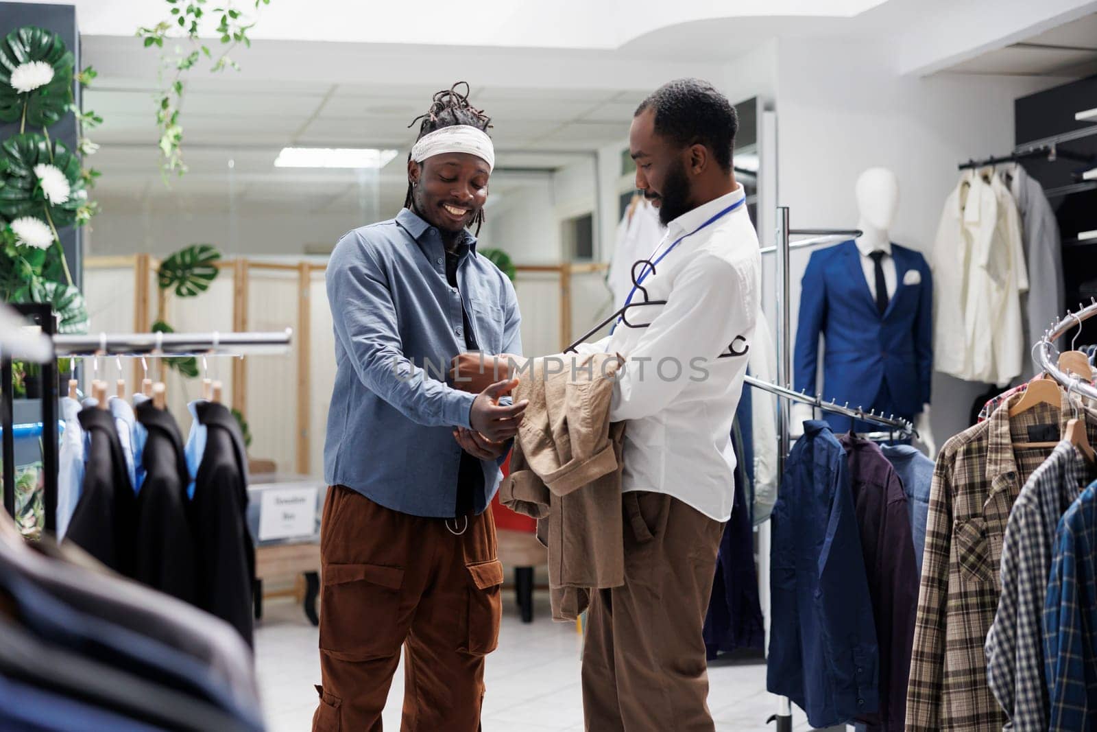 Smiling man trying on shirt and discussing with salesperson by DCStudio