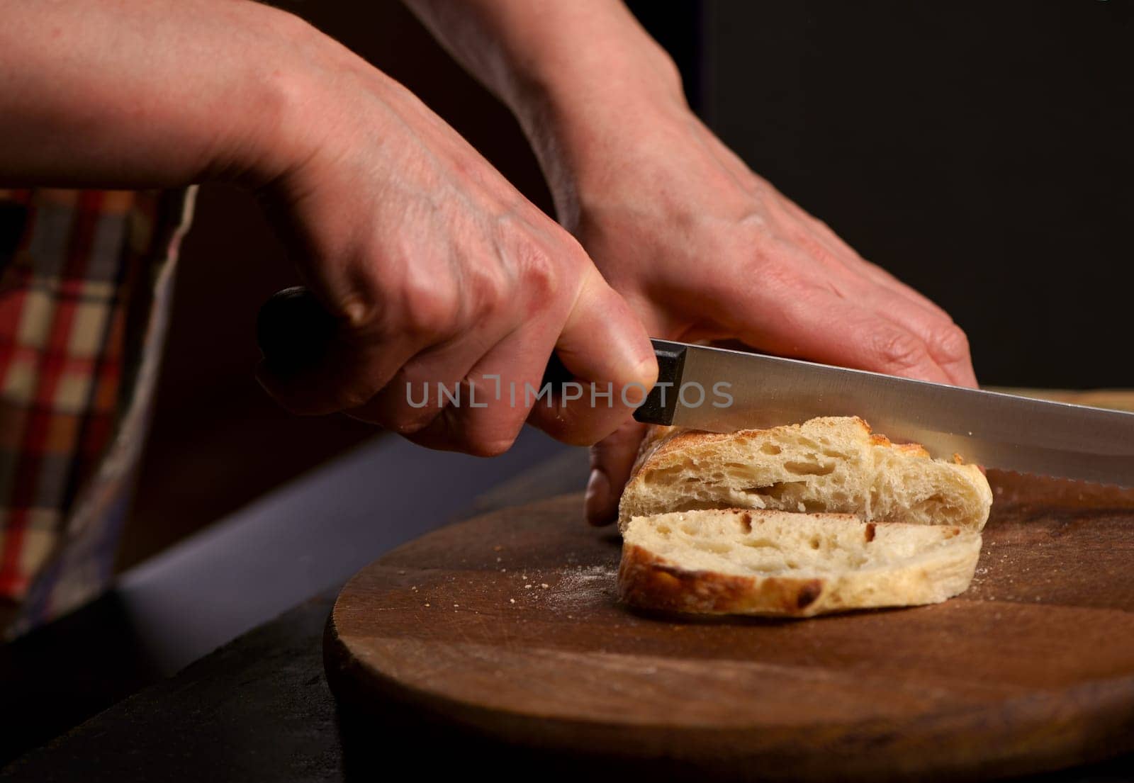 The healthy eating and traditional bakery concept. Front viev. Whole grain bread put on kitchen wood plate with a chef holding knife for cut. Fresh bread on table close-up. Fresh bread on the kitchen table