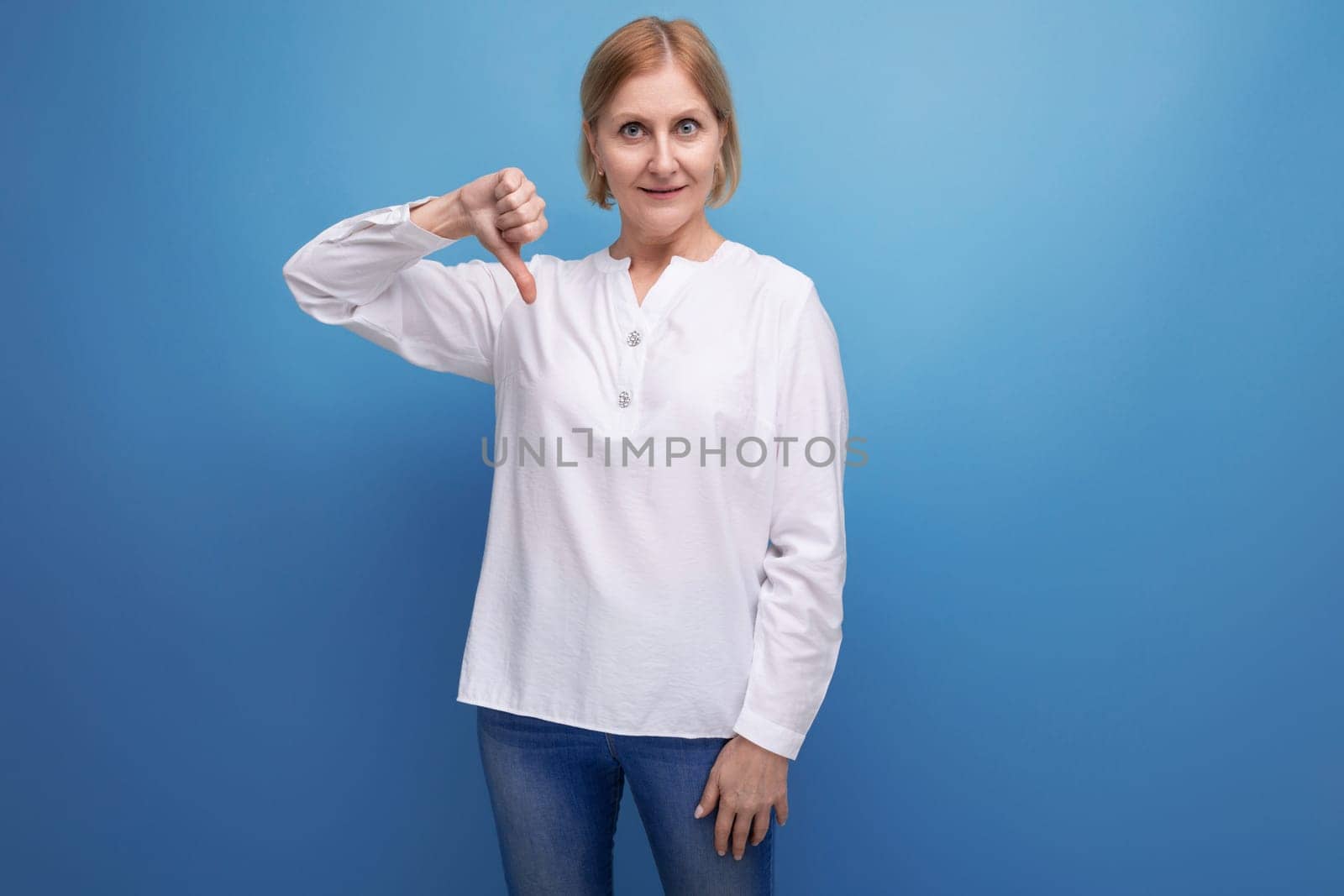 serious blond middle aged woman in white blouse showing dislike on studio background.
