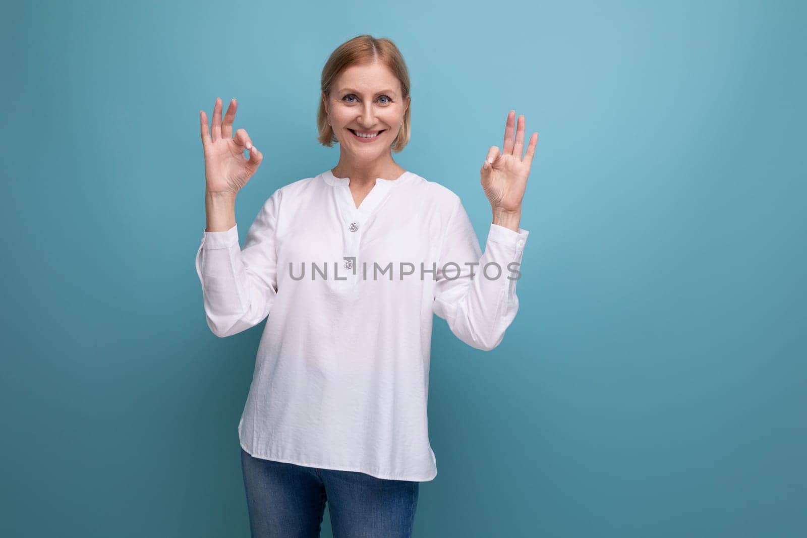 kind pleasant blond mature woman with clean face at menopause age in studio background.