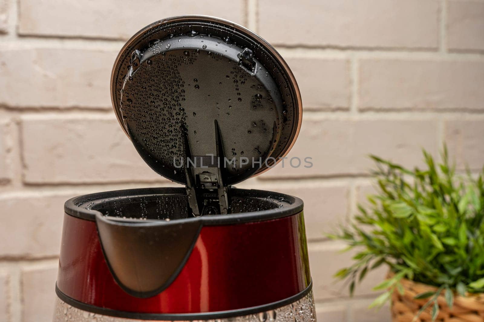 a new modern electric kettle with an open lid and drops of condensate on it, with boiling water against a light brick wall. close-up