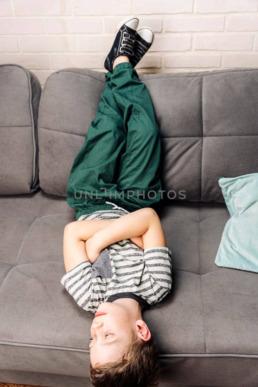 The child is lying in classic sneakers on a cozy sofa in the living room, with his feet on the back of the sofa, resting and relaxing. comfortable casual clothes and shoes.the child is lying upside down