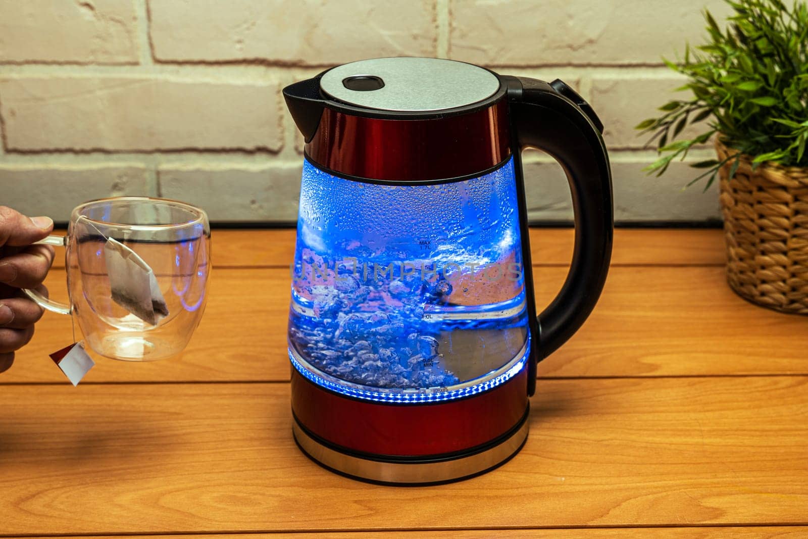 Brewing a tea bag. a fashionable tea cup with double glass walls and a modern electric transparent teapot with bubbling water and blue neon lighting on the table close-up.