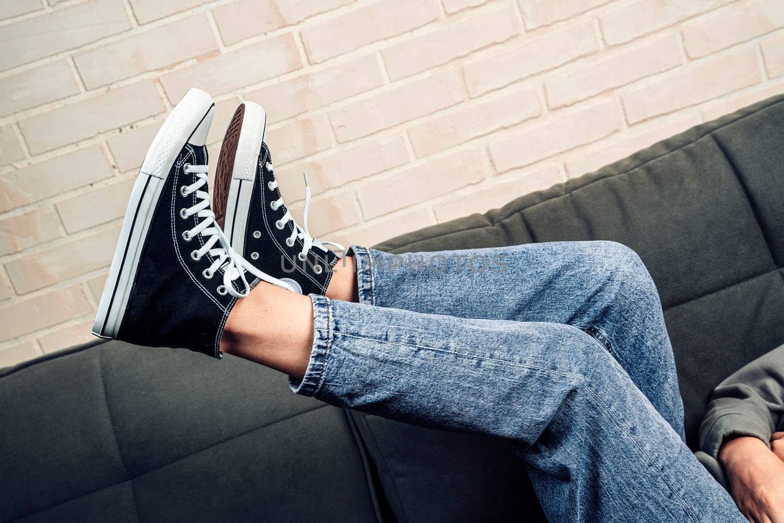 the girl's legs shod in classic sneakers. A sneakers on a girl's leg. Teenager's feet in casual new sneakers on the sofa close up image. Vintage style. concept image. Female feet in jeans and sports shoes