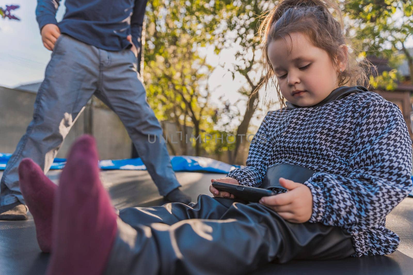 portrait of children who sit on a trampoline and look at the phone