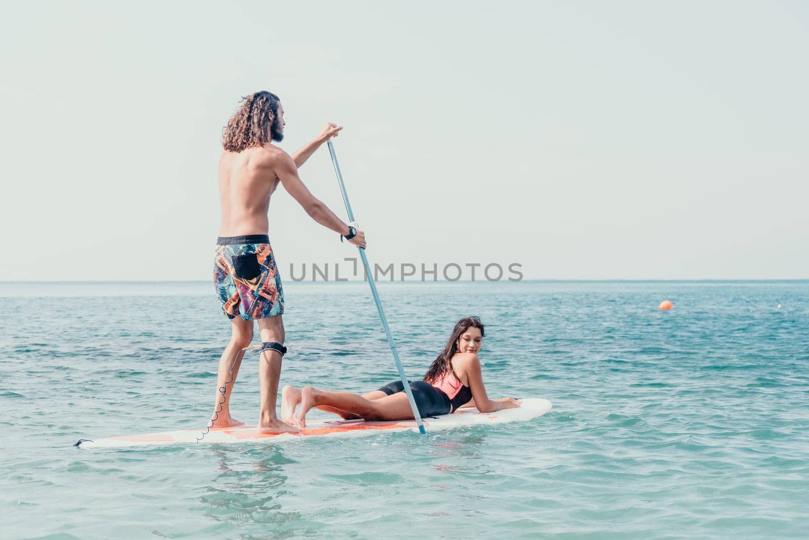 Silhouette of woman standing, surfing on SUP board, confident paddling through water surface. Idyllic sunset or sunrise. Sports active lifestyle at sea or river.