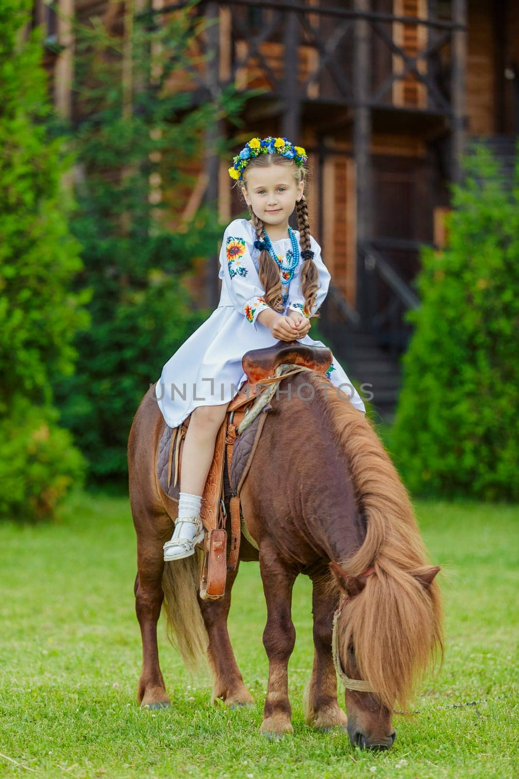 A little girl in the Ukrainian national costume rides a pony on the lawn