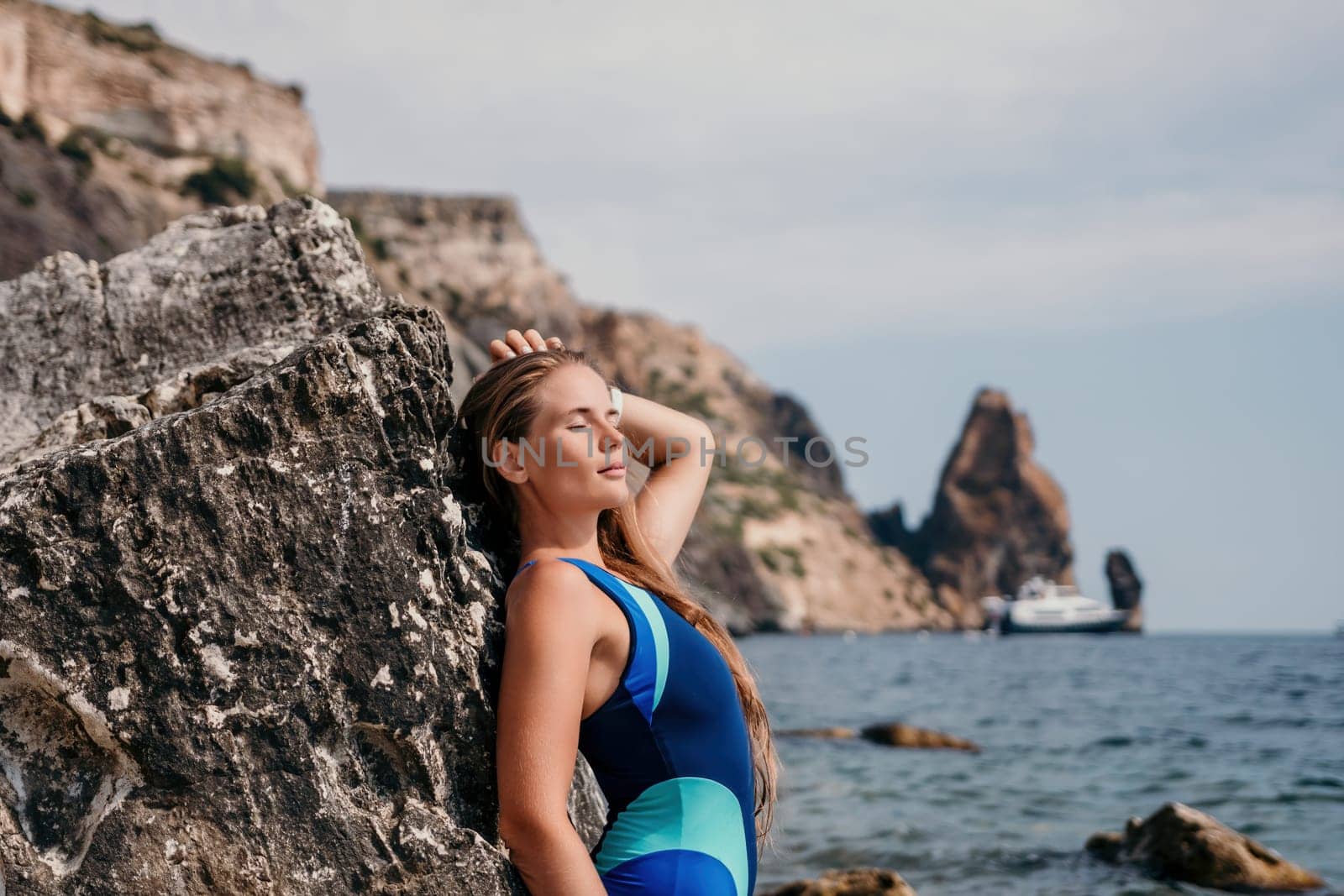 happy tourist in blue swimwear takes a photo outdoors to capture memories. The photo depicts a woman traveling and enjoying her surroundings on the beach, with volcanic mountains in the background