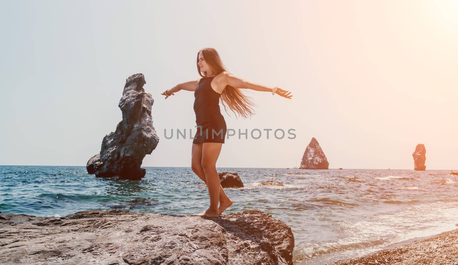 Woman travel sea. Young Happy woman in a long red dress posing on a beach near the sea on background of volcanic rocks, like in Iceland, sharing travel adventure journey