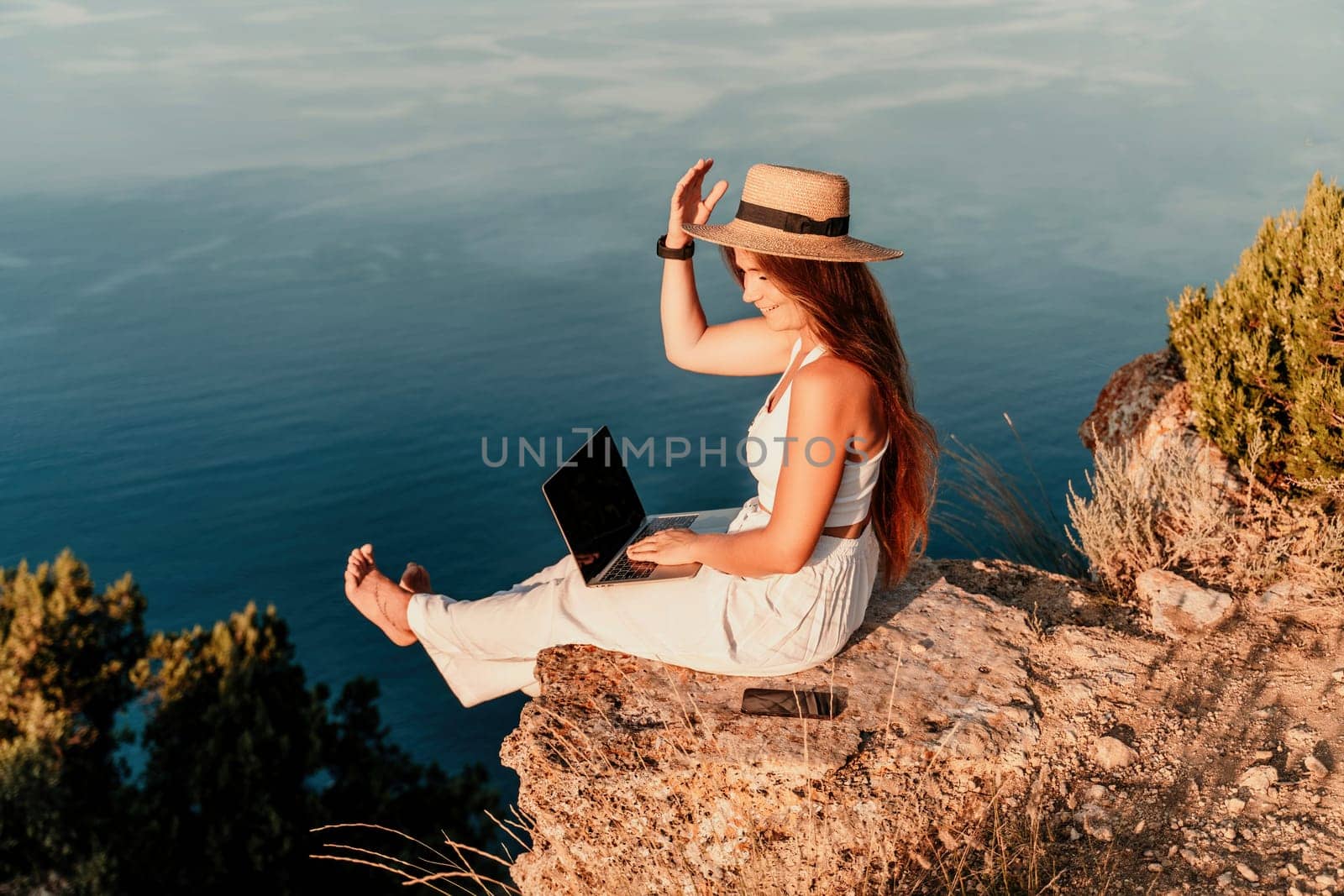 Freelance women sea working on the computer. Good looking middle aged woman typing on a laptop keyboard outdoors with a beautiful sea view. The concept of remote work