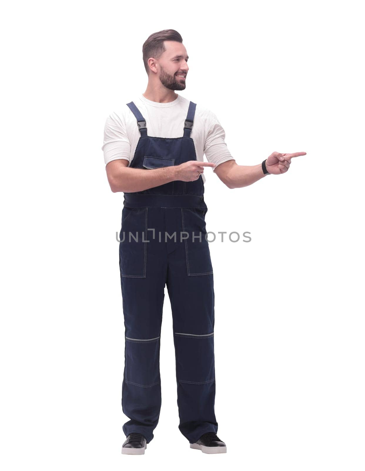in full growth. smiling man in overalls pointing to a copy of the space . isolated on white
