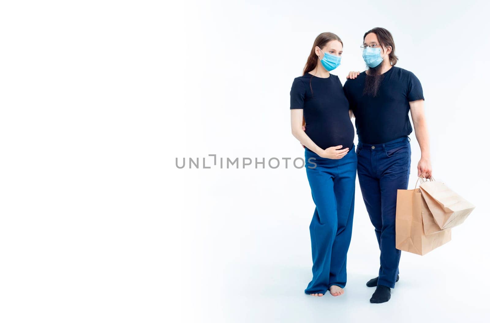young pregnant woman and her husband with shopping bags in medical masks. safety from colds flu and coronavirus on white background. Pregnancy shopping concept happy young family with shopping bags