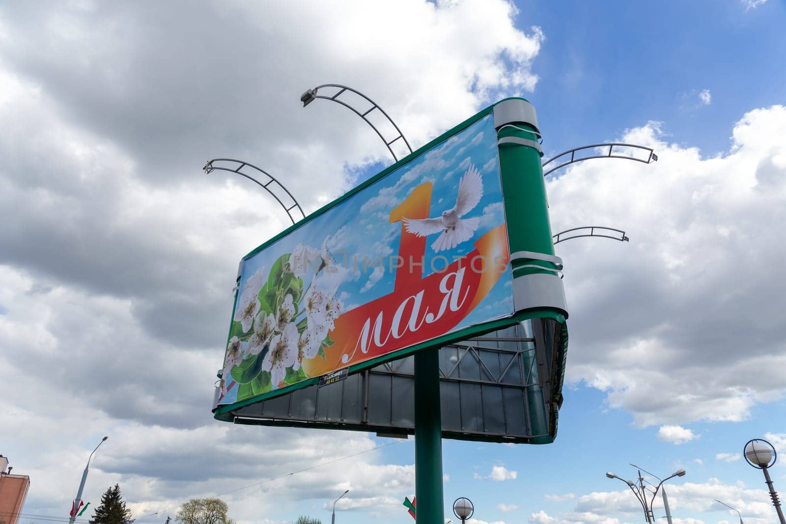 Grodno, Belarus - 24 April, 2023: A billboard with congratulations on the International Labor Day on May 1 in the form of apple blossoms, a dove and a red ribbon on a blue sky background with white flowers on the Gorky street.