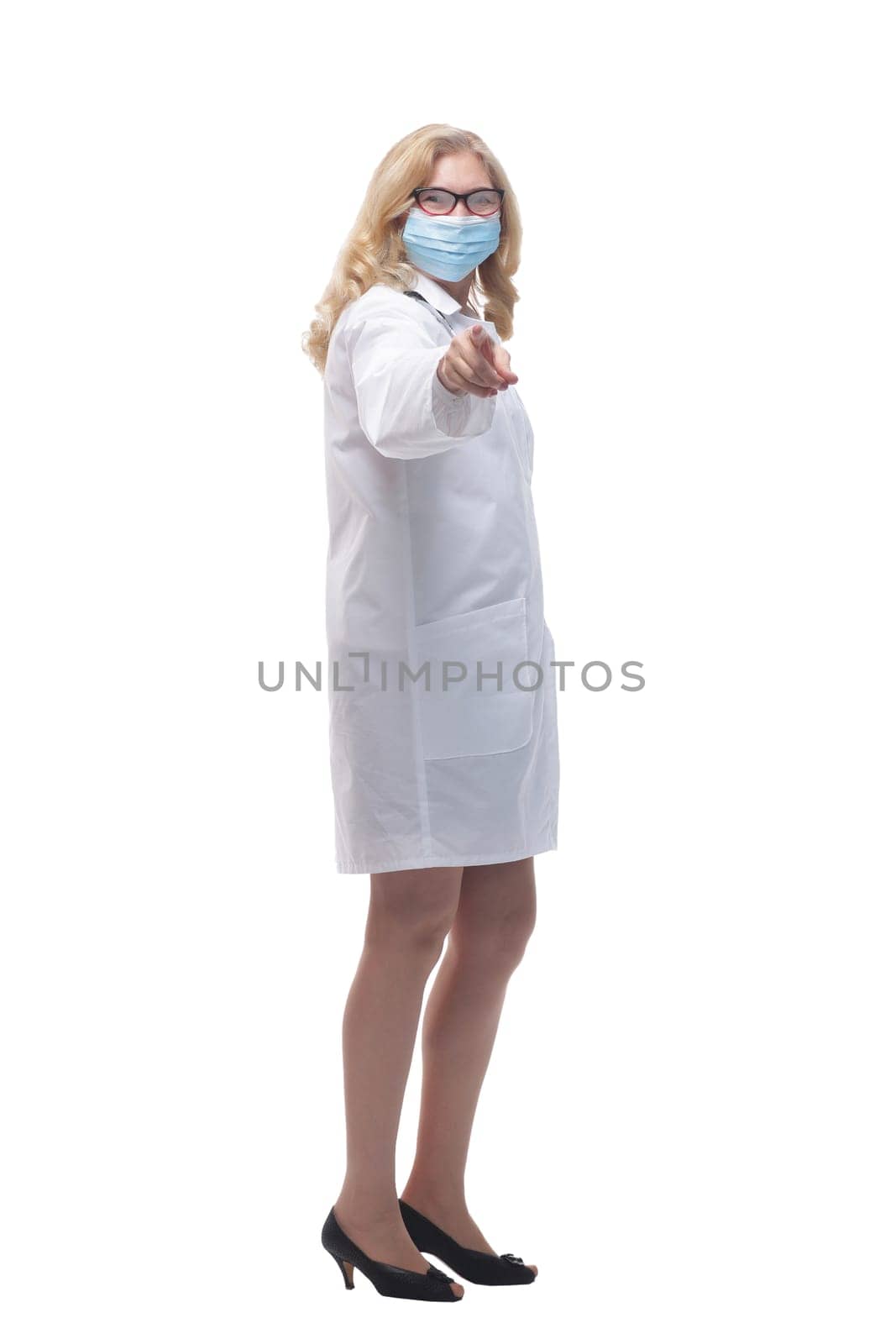 in full growth. female doctor in a protective mask pointing at you. isolated on a white background.