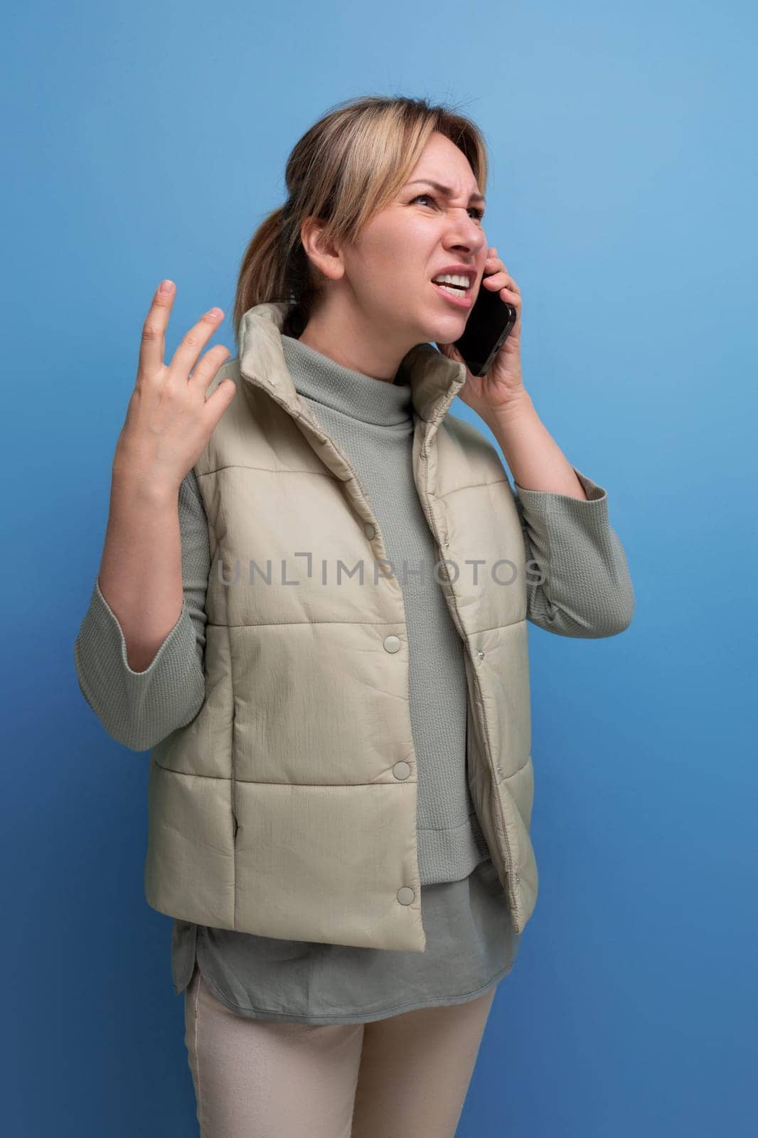 blond millennial woman talking on the phone on a blue isolated background.